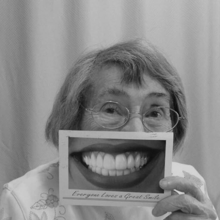 Fotografia em preto e branco em close do rosto de uma pessoa sorrindo amplamente com os olhos semicerrados, destacando detalhes como textura da pele, cílios e dentes.